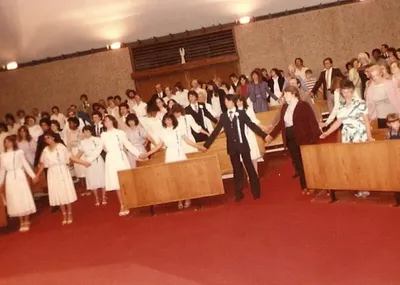 A view of the seating in the former church. The angel in the background now resides over the entrance of the present church. Appears to be from a Confirmation Mass. Source: Unknown.