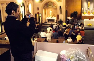 Woman taking a photograph during the closing Mass. View of the left side of the church. Source: Catholic Courier