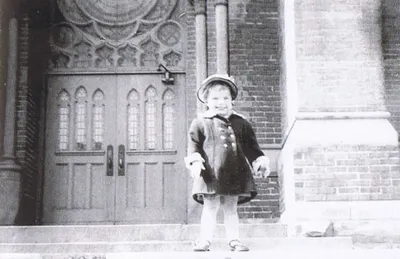 Child standing outside of the main entrance to St. Boniface, 1953. The stained glass windows above the door are somewhat visible in this photograph. Source: Images of America, Southeast Rochester