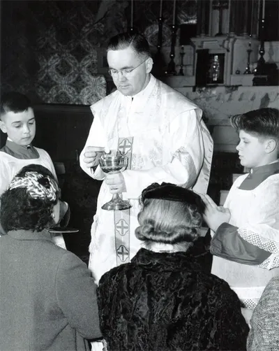 Fr. Donovan distriuting Communion in the original church. High altar can be sign in the background.